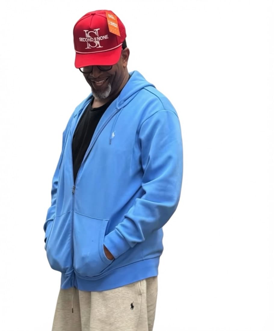 Person in a blue zip hoodie wearing a red Second II None cap